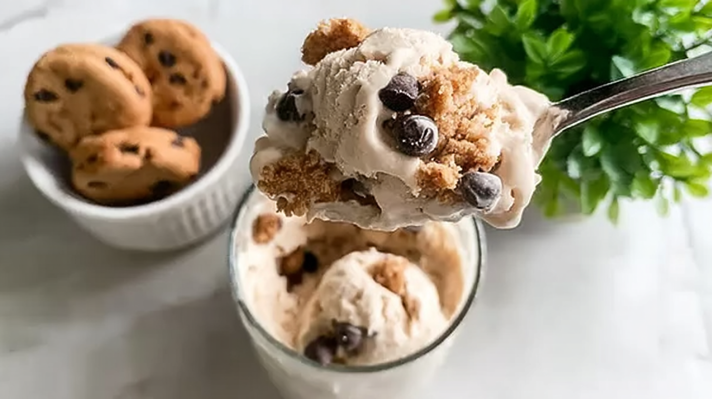 A spoonful of creamy Ninja Creami protein ice cream mixed with chocolate chips and cookie dough pieces, held over a glass.